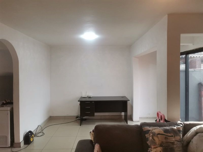 A living area featuring neutral tiled flooring and an arched architectural doorway, providing a blank canvas for interior design.