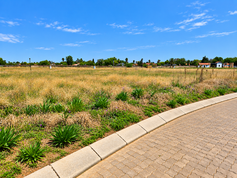 A vacant residential plot featuring a paved driveway edge, concrete curbing, and established perimeter boundary walling.