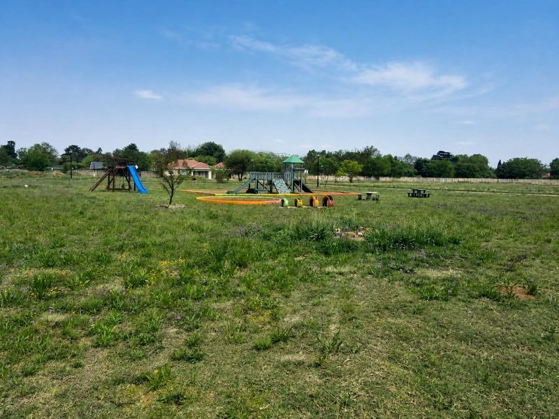 A spacious residential garden area featuring an established playground set and open grass lawn.