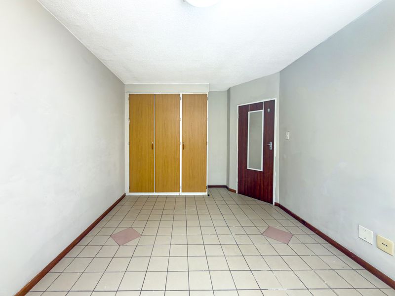 An empty bedroom featuring tiled flooring, built-in wooden cupboards, and a single entry door.