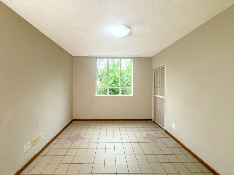 A vacant bedroom featuring neutral walls, tiled flooring, a security gate, and a window providing natural light.