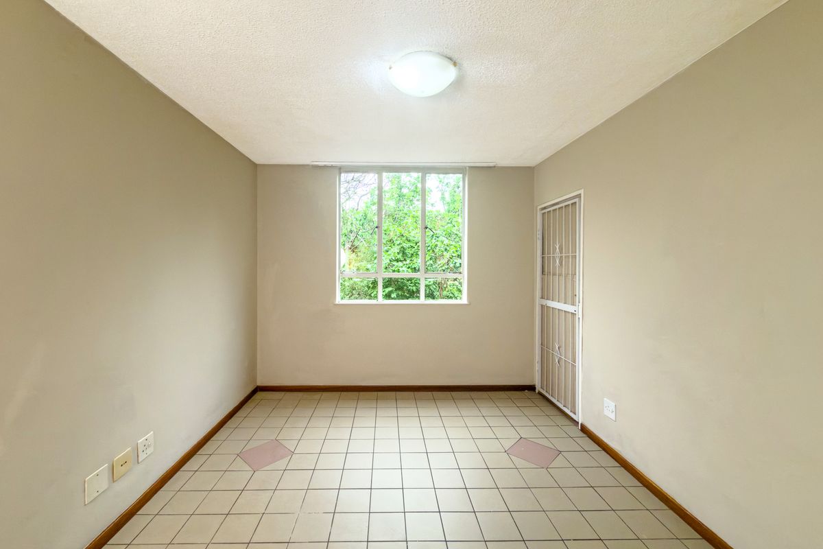 A vacant bedroom featuring neutral walls, tiled flooring, a security gate, and a window providing natural light.