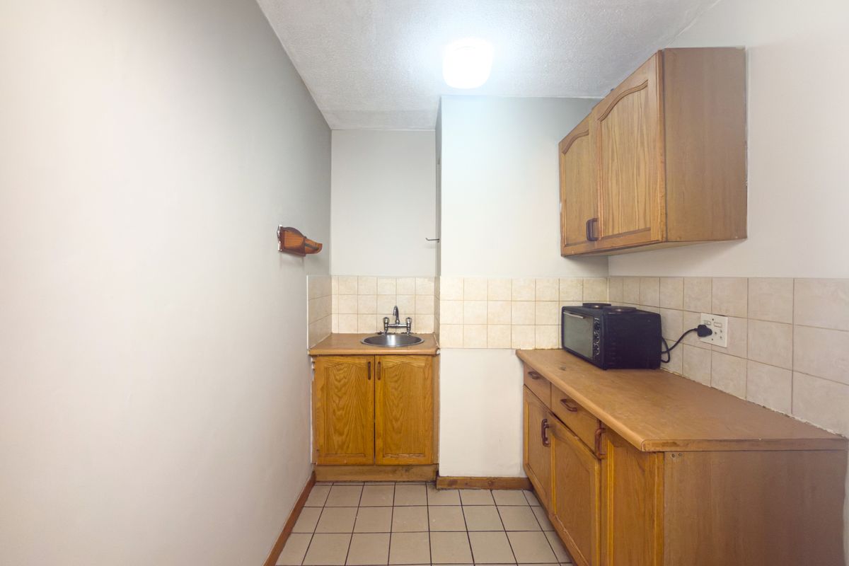 A compact kitchen featuring wooden cabinetry, tiled backsplash, and tiled flooring, offering a functional space ready for modernization.