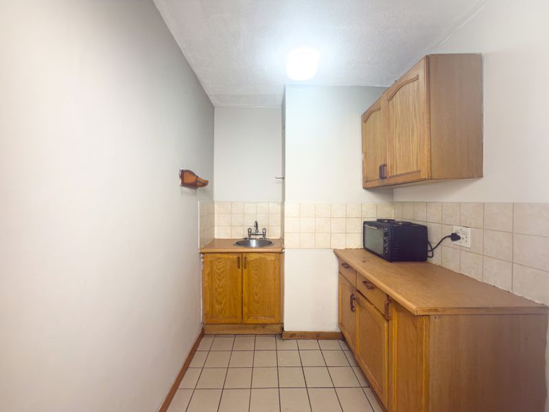A compact kitchen featuring wooden cabinetry, tiled backsplash, and tiled flooring, offering a functional space ready for modernization.