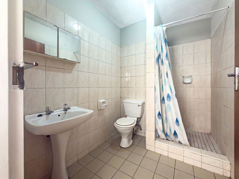 A functional bathroom featuring a pedestal basin, toilet, and a tiled shower cubicle with a curtain. The space is ready for modernization.