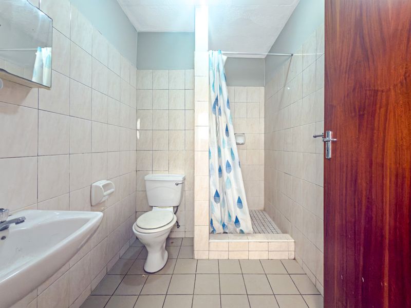 A functional bathroom featuring a pedestal basin, toilet, and a tiled shower cubicle with a curtain rail, finished with neutral wall and floor tiles.