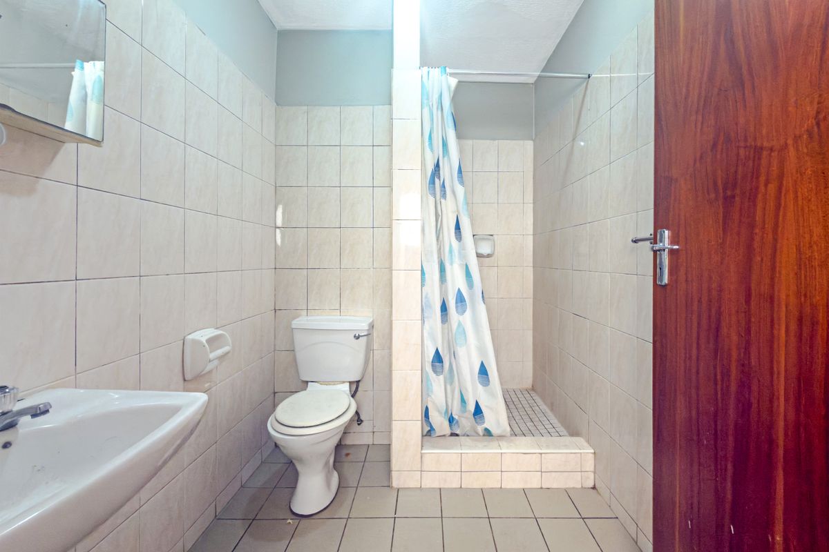 A functional bathroom featuring a pedestal basin, toilet, and a tiled shower cubicle with a curtain rail, finished with neutral wall and floor tiles.