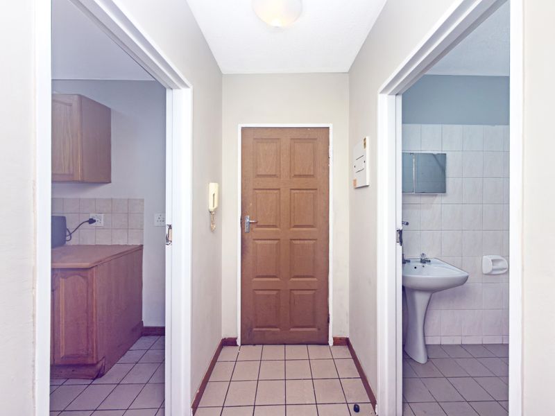 A functional hallway providing access to a kitchen and bathroom, featuring tiled flooring and basic built-in fixtures.