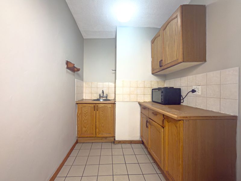 A functional scullery area featuring built-in wooden cabinetry, a stainless steel sink, and tiled backsplash, offering potential for modernization.