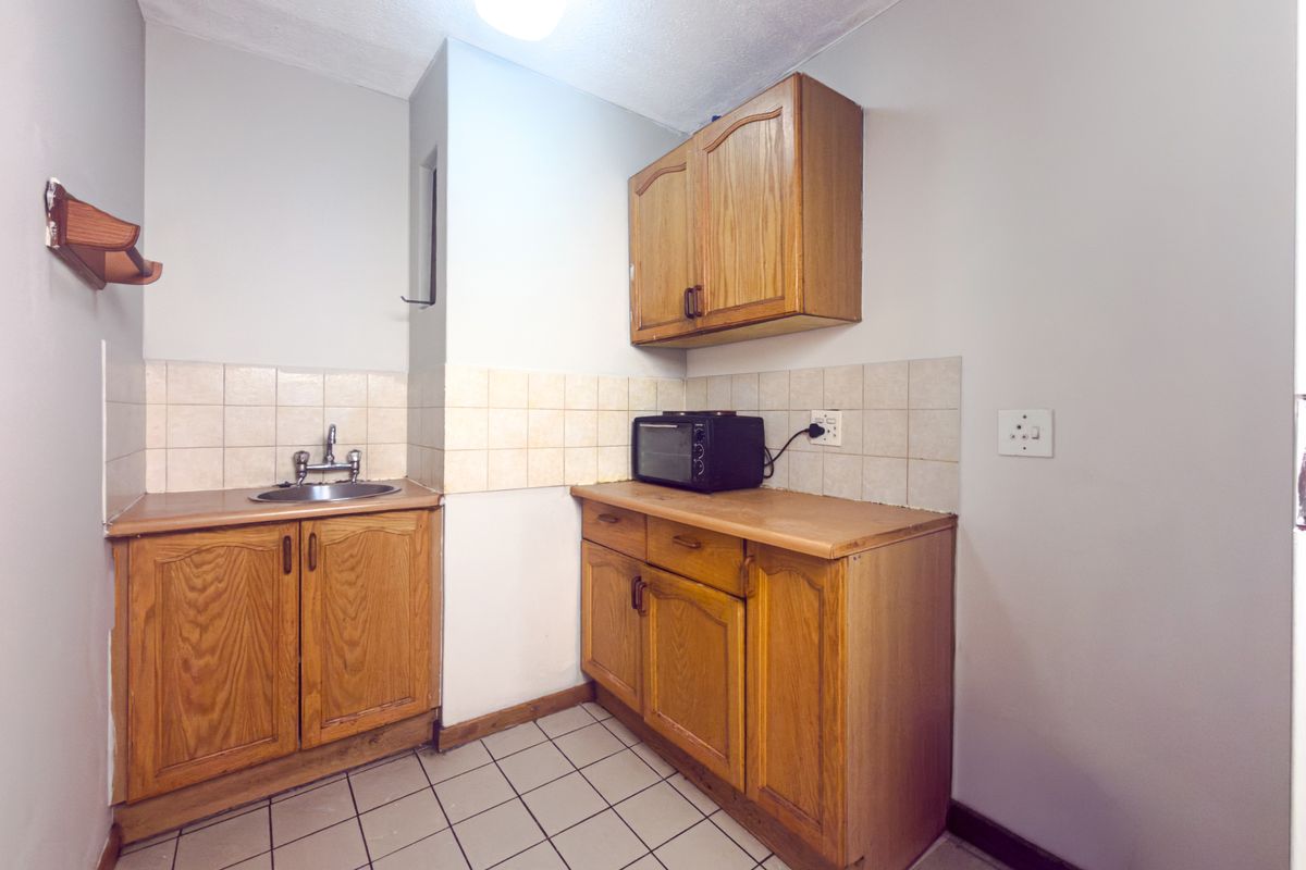 A compact kitchen featuring wooden cabinetry, tiled splashbacks, and tiled flooring, offering a functional space with potential for modern updates.