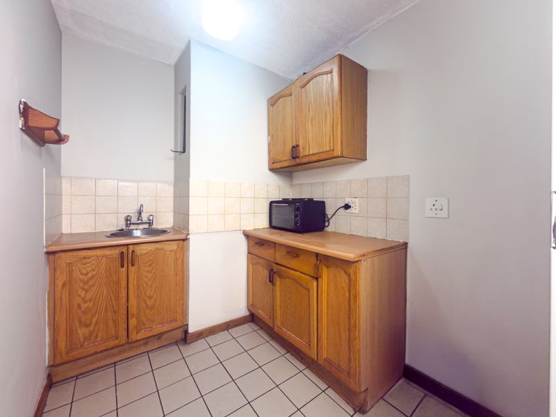 A compact kitchen featuring wooden cabinetry, tiled splashbacks, and tiled flooring, offering a functional space with potential for modern updates.