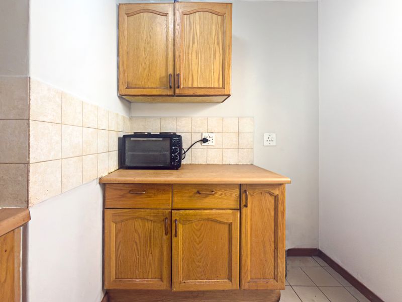A compact kitchen area featuring dated wooden cabinetry, laminate countertops, and neutral ceramic wall and floor tiling.