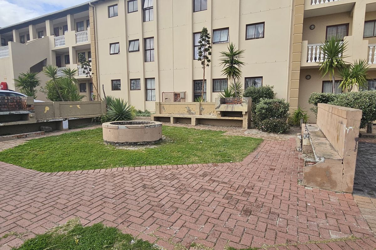 Communal outdoor courtyard area featuring paved walkways, built-in brick braai facilities, and concrete seating within an apartment complex.