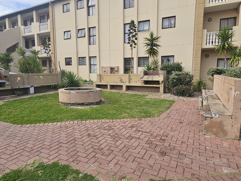 Communal outdoor courtyard area featuring paved walkways, built-in brick braai facilities, and concrete seating within an apartment complex.