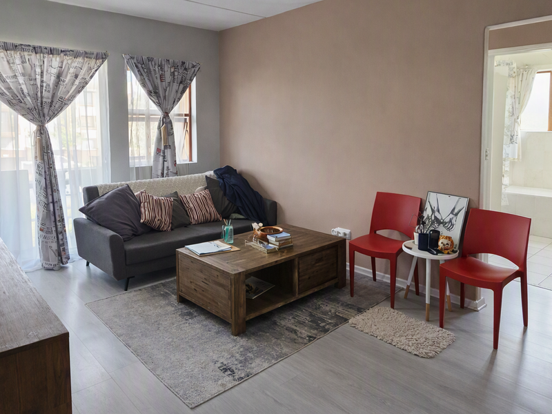 A well-lit living room featuring light-toned laminate flooring and neutral wall finishes, providing a comfortable and functional space with direct access to adjacent areas.