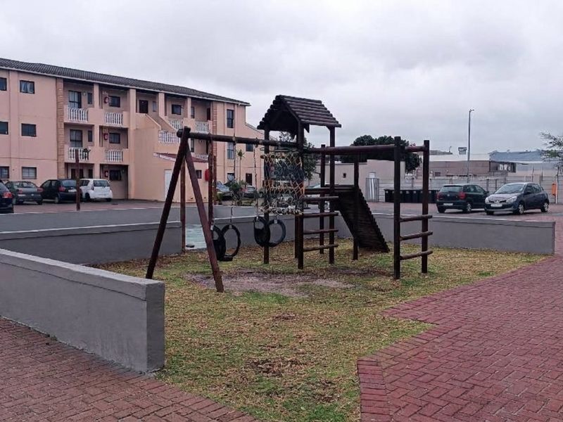 Communal outdoor area featuring a paved driveway, retaining walls, and a playground structure within an apartment complex setting.