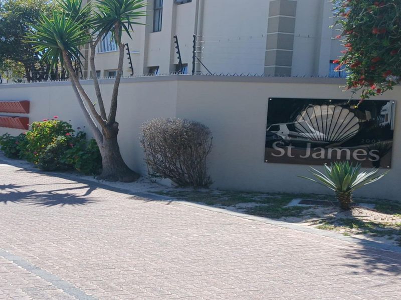 Street-level view of the St James apartment complex entrance, featuring a secure perimeter wall with electric fencing and paved driveway access.