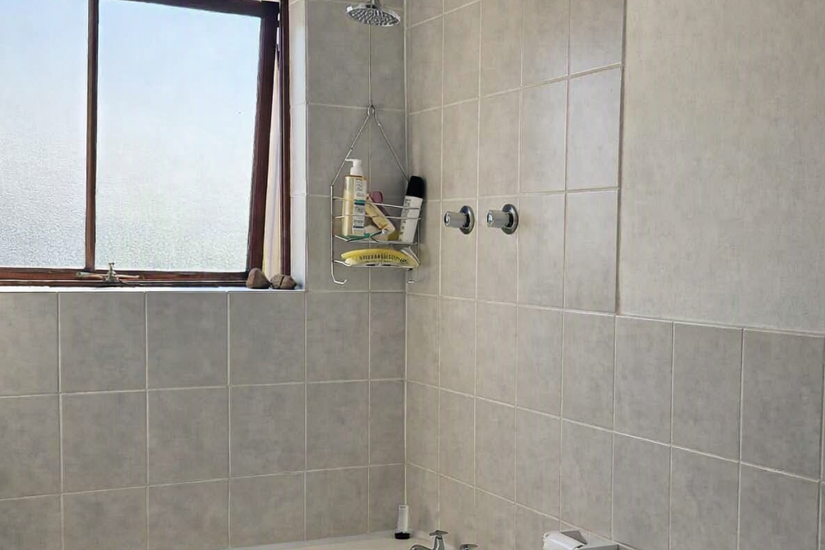A functional bathroom featuring a bathtub with shower head, tiled walls, and a toilet, showing signs of wear on the ceiling and wall finishes.