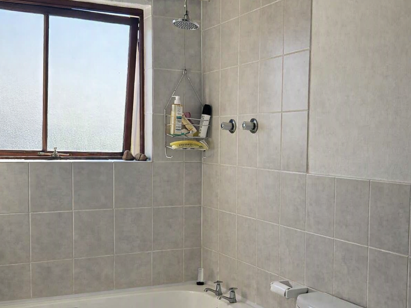 A functional bathroom featuring a bathtub with shower head, tiled walls, and a toilet, showing signs of wear on the ceiling and wall finishes.