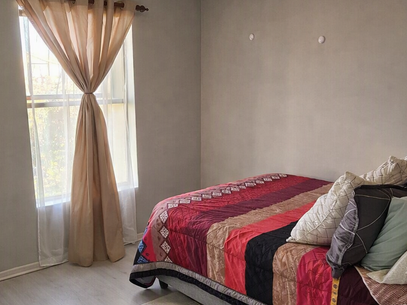 A bedroom featuring light-toned laminate flooring and a single window with neutral wall finishes.