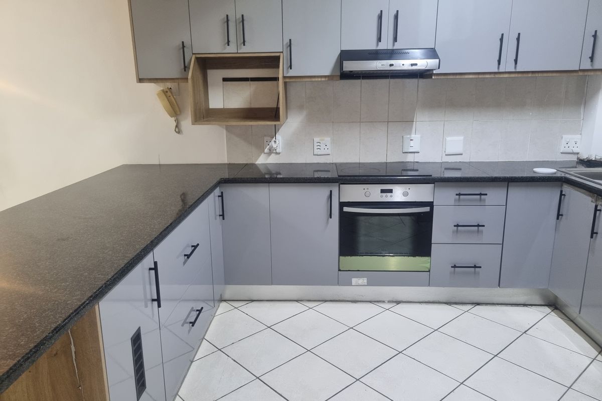 Modern kitchen featuring grey cabinetry, granite countertops, built-in oven, electric hob, and extractor fan with tiled flooring and backsplash.