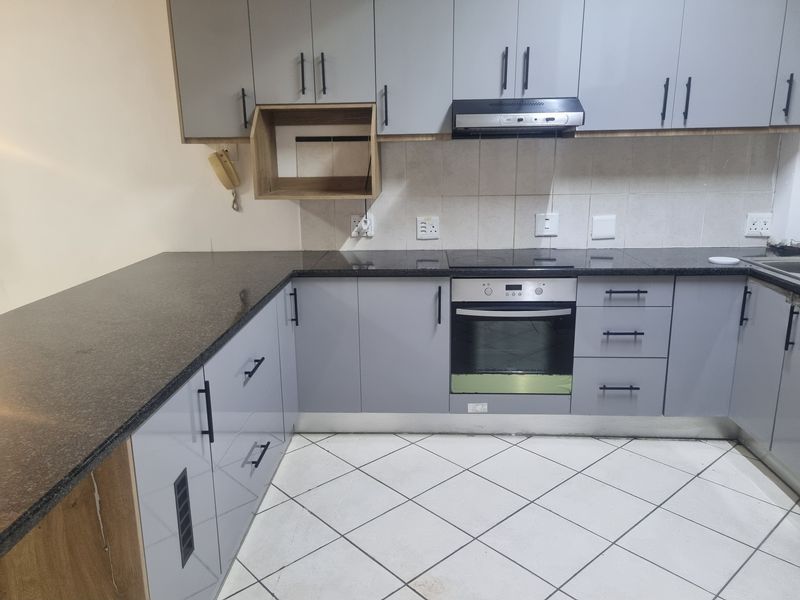 Modern kitchen featuring grey cabinetry, granite countertops, built-in oven, electric hob, and extractor fan with tiled flooring and backsplash.