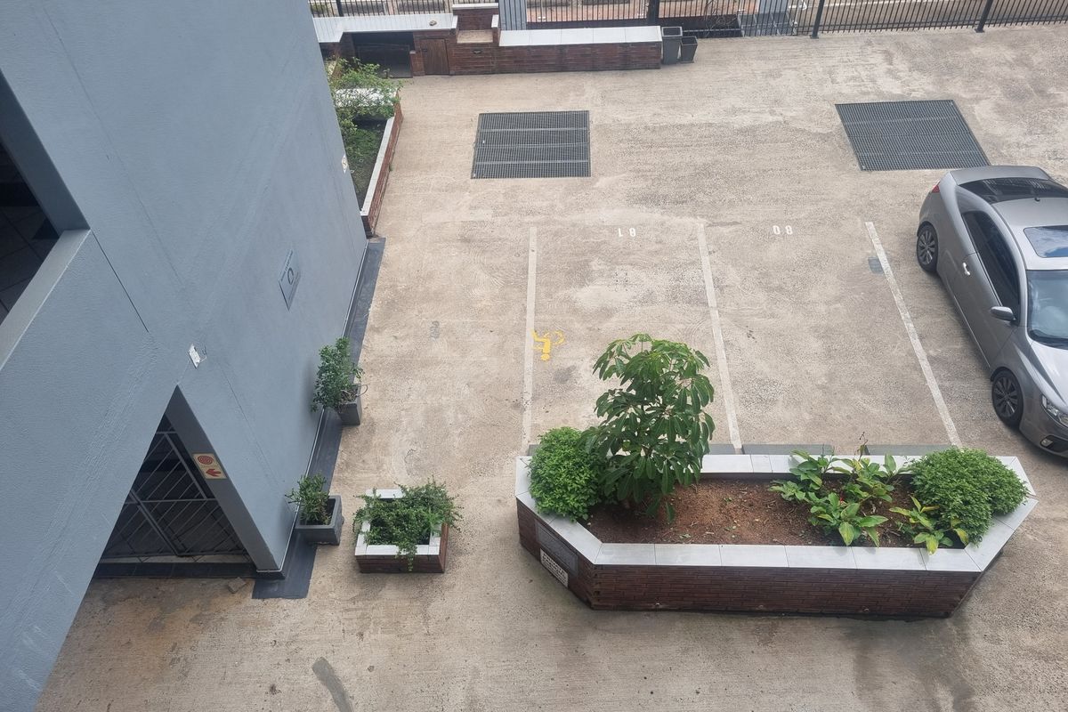 An elevated view of the apartment complex rear parking area featuring paved bays, brick planter boxes, and a built-in outdoor counter.