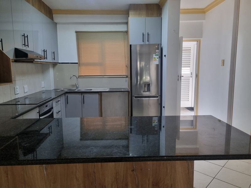 Modern kitchen featuring granite countertops, ample built-in cabinetry, stainless steel sink, built-in oven, and extractor fan with tiled flooring.