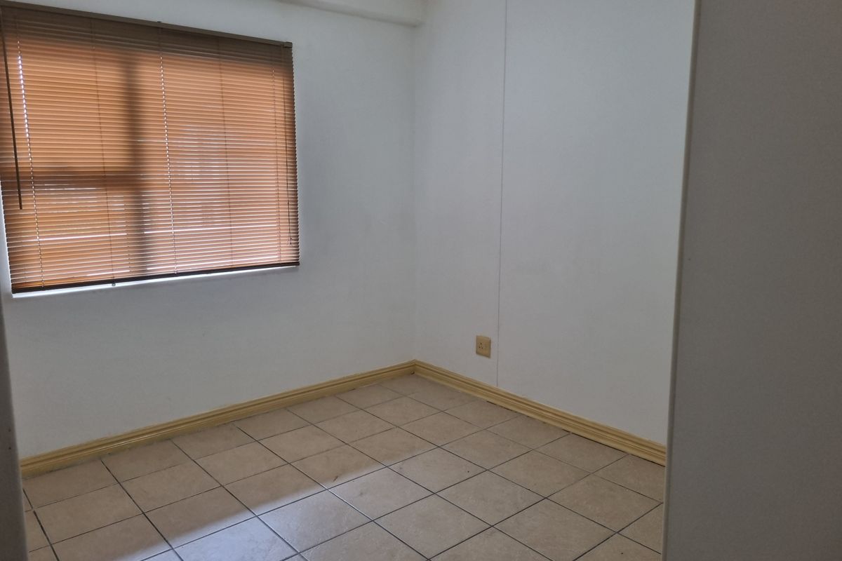 An empty bedroom featuring neutral tiled flooring, white walls, and fitted venetian blinds, offering a clean and versatile space ready for personalization.