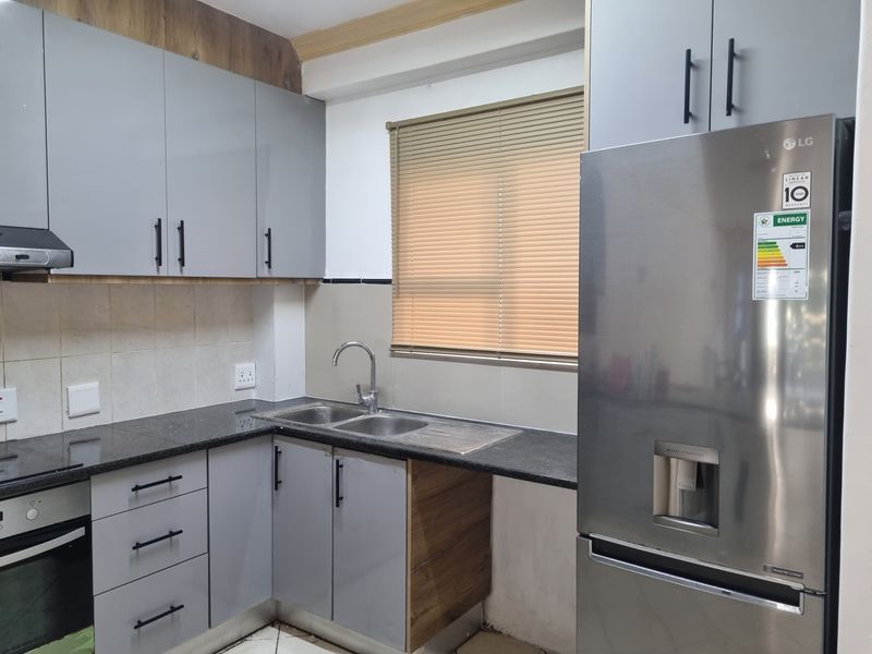 A functional kitchen featuring grey cabinetry, granite countertops, a double basin sink, built-in oven, and extractor fan, complemented by a tiled backsplash and venetian blinds.