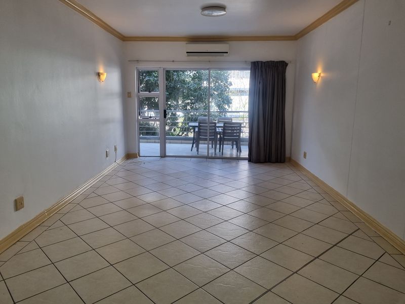 An empty living room featuring ceramic tile flooring, wall-mounted air conditioning, and sliding glass doors leading to an outdoor balcony area.