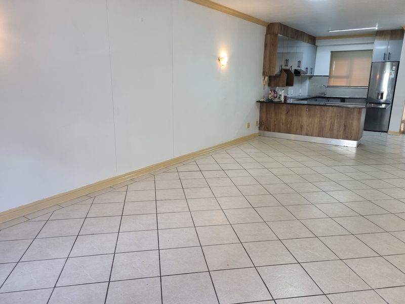 An open-plan living and kitchen area featuring tiled flooring, wood-finish cabinetry, granite countertops, and neutral wall finishes in a vacant apartment setting.