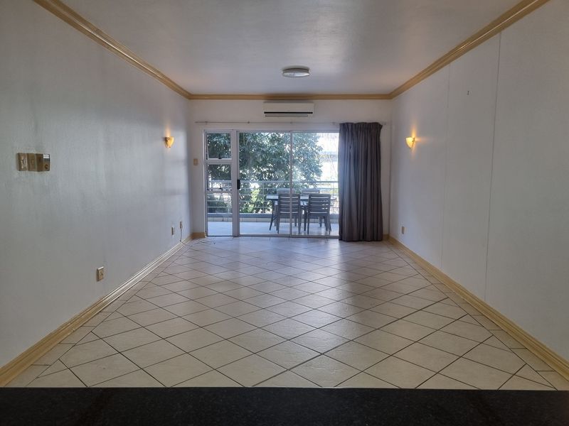 An empty, open-plan living area featuring tiled floors, crown molding, and a sliding glass door leading to a balcony with air conditioning.