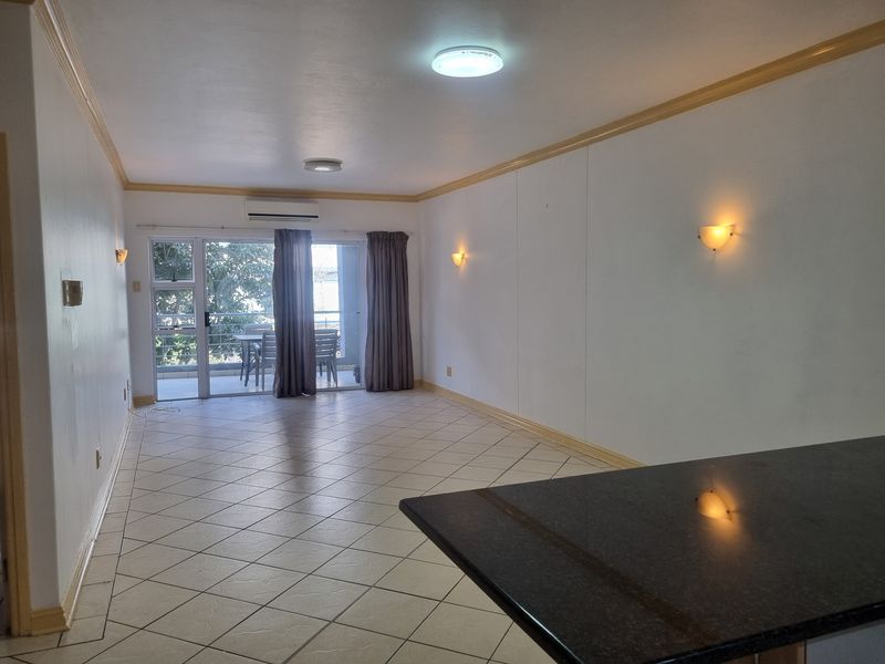Spacious open-plan living area featuring tiled floors, granite breakfast bar, wall-mounted air conditioning, and sliding glass doors leading to a balcony.