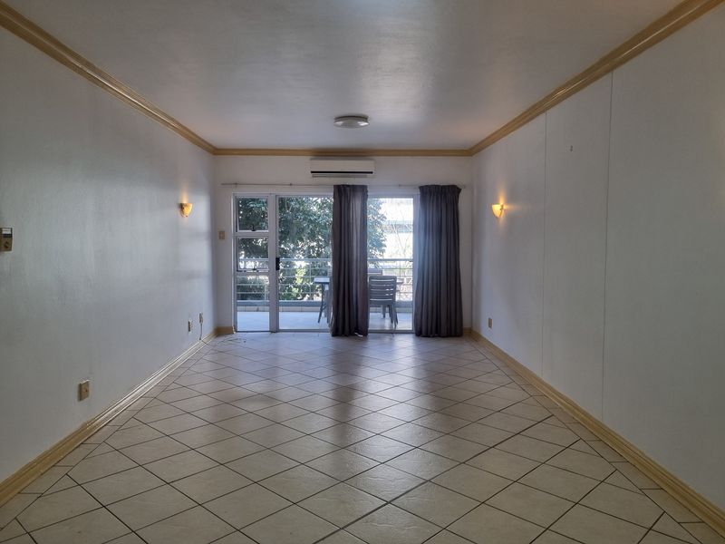 An empty, well-lit living room featuring tiled floors, crown molding, wall sconces, and a split-system air conditioner, with direct access to a balcony.