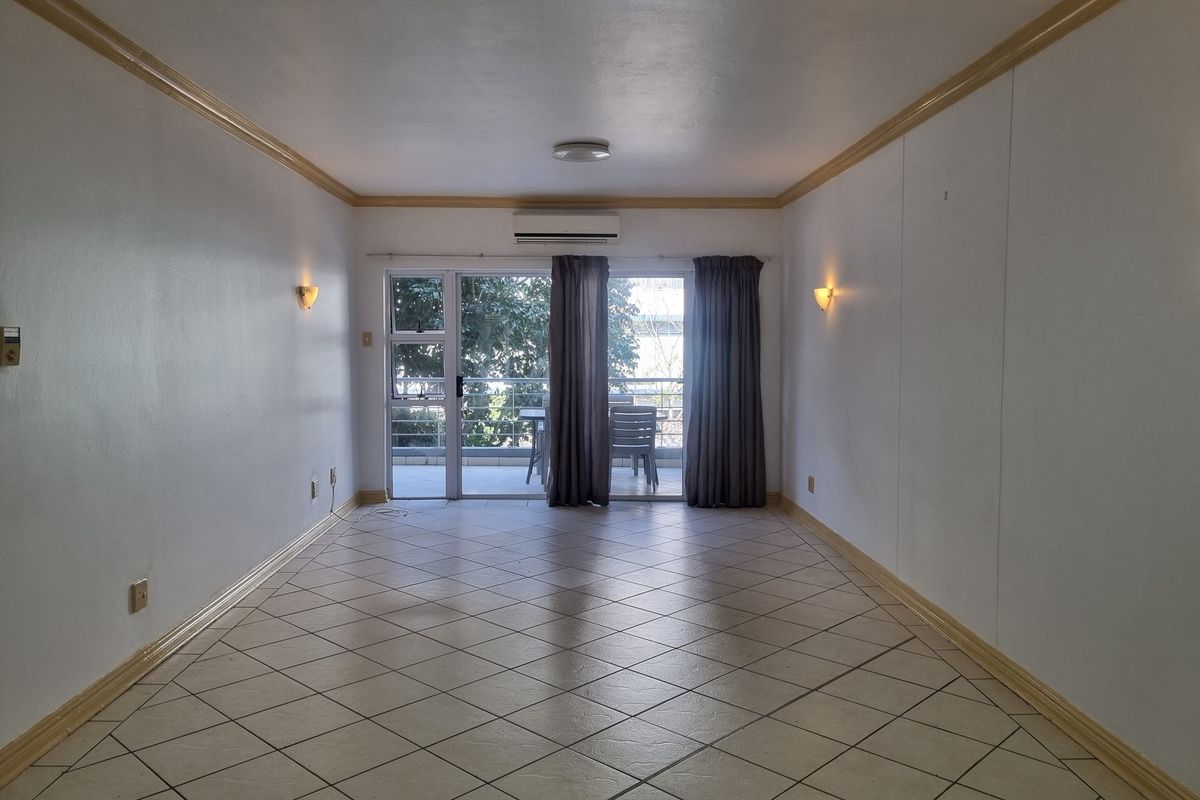 An empty, well-lit living room featuring tiled floors, crown molding, wall sconces, and a split-system air conditioner, with direct access to a balcony.