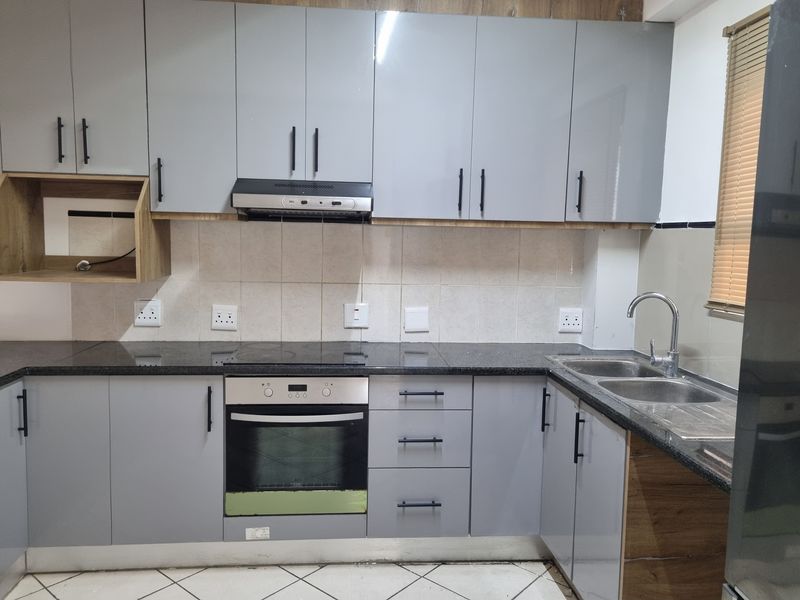 Modern kitchen featuring grey cabinetry, black granite countertops, built-in oven, electric hob, extractor fan, and a double bowl stainless steel sink.