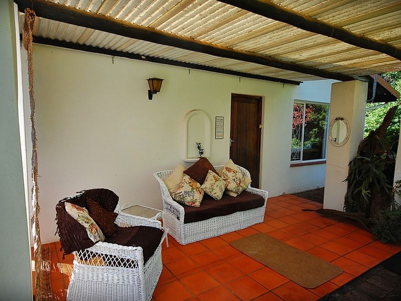 A covered outdoor patio featuring terracotta floor tiles, a corrugated roof, and a recessed wall niche, providing a functional space for outdoor relaxation.