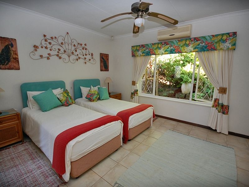 A bedroom featuring tiled flooring, a ceiling fan, and a wall-mounted air conditioning unit, with a window overlooking the garden.