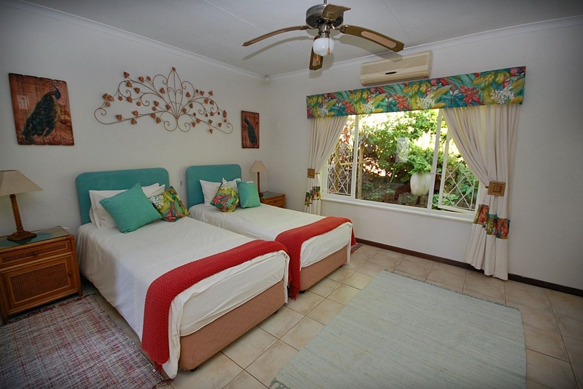 A bedroom featuring tiled flooring, a ceiling fan, and a wall-mounted air conditioning unit, with a window overlooking the garden.