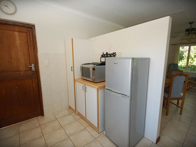 A functional kitchen area featuring tiled flooring, built-in cabinetry with laminate countertops, and a solid timber door, providing a practical layout.