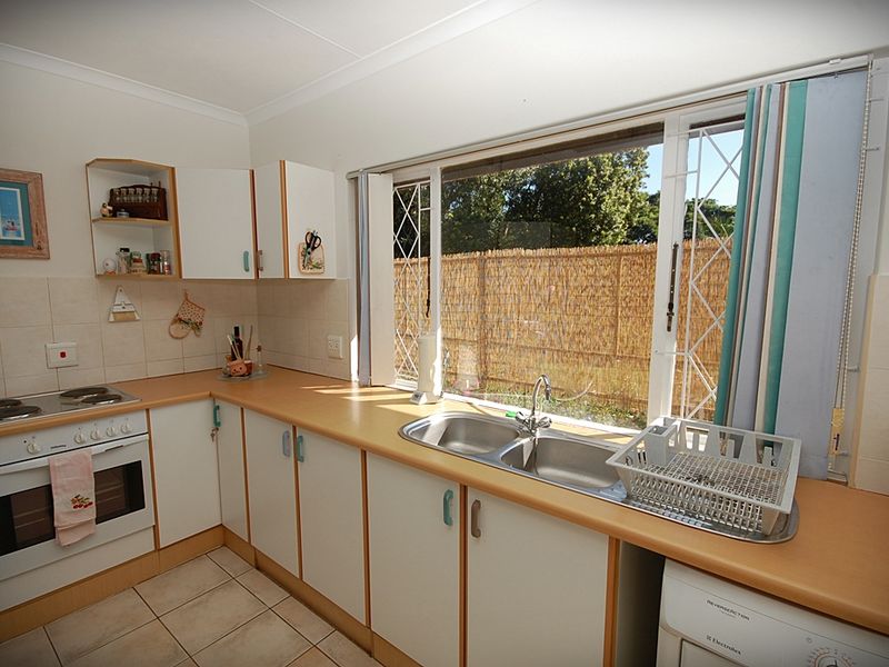 A functional kitchen featuring white cabinetry, laminate countertops, a double sink, and built-in electric cooking appliances with a view to the rear garden.