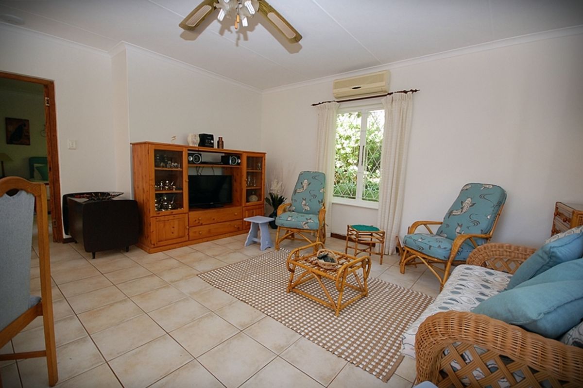 A comfortable living room featuring tiled flooring, a ceiling fan, and a wall-mounted air conditioning unit, with natural light from a leaded glass window.