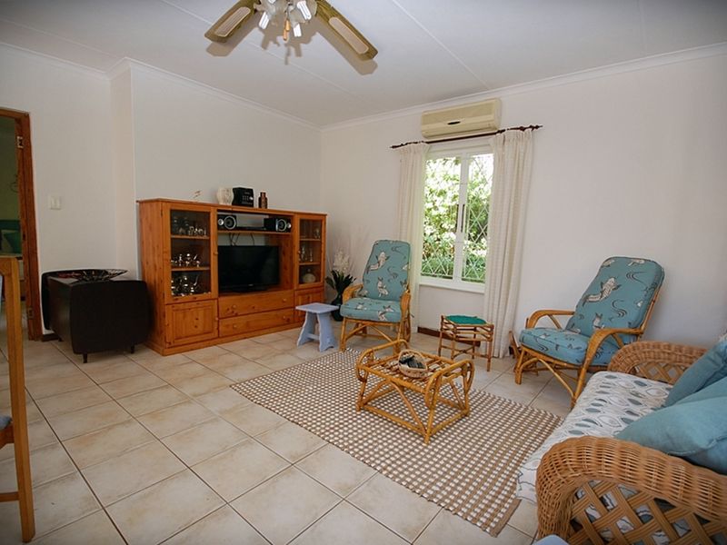 A comfortable living room featuring tiled flooring, a ceiling fan, and a wall-mounted air conditioning unit, with natural light from a leaded glass window.