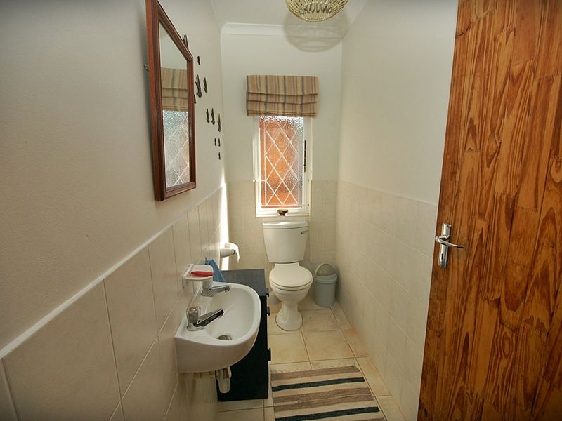 A compact guest bathroom featuring a wall-mounted basin, toilet, tiled splashbacks, and a leaded glass window.