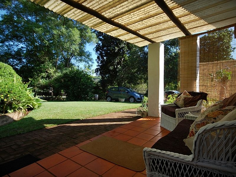 A covered patio area featuring terracotta tiling and a corrugated roof, overlooking a lush green garden and lawn.