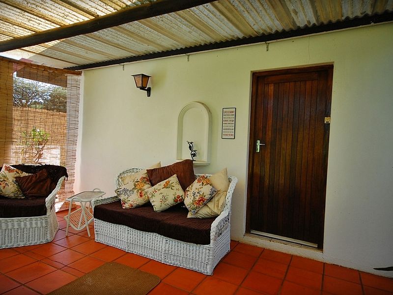 A covered outdoor patio featuring terracotta floor tiles, a timber entrance door, and a corrugated roof structure.