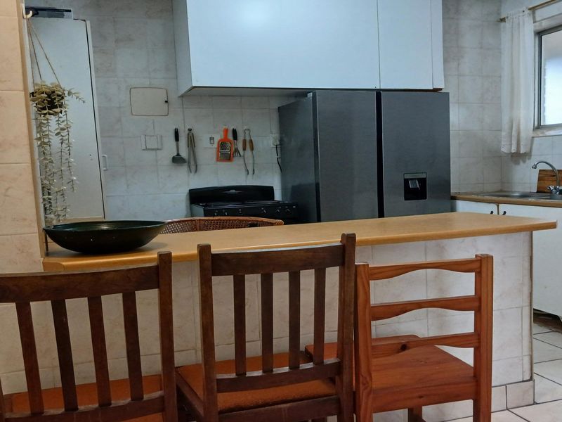 A functional kitchen featuring a breakfast bar, tiled backsplash, built-in cabinetry, and a double sink, offering a practical layout for daily use.