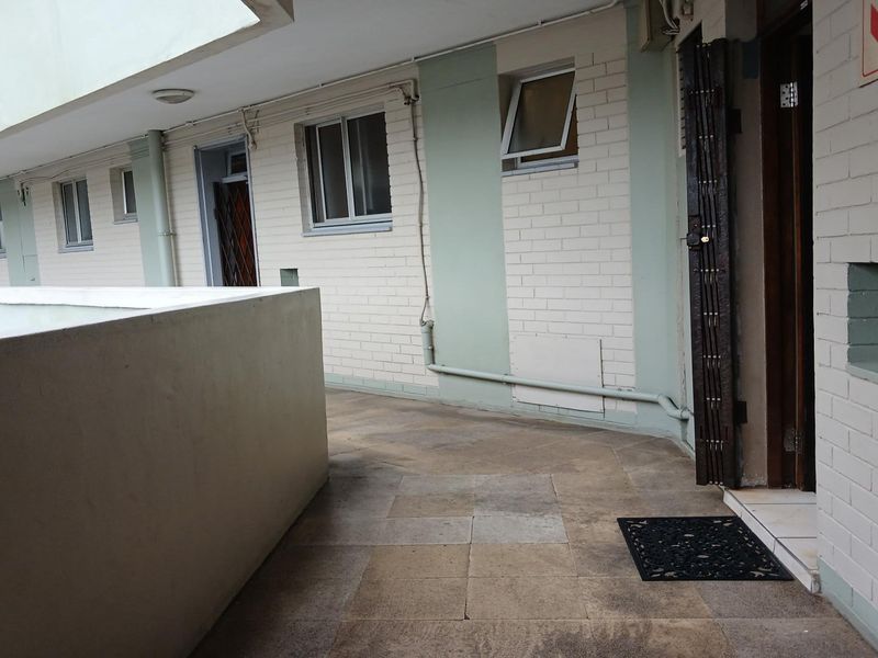 A view of the exterior walkway and building facade featuring brickwork, security gates, and tiled flooring in a residential flat complex.