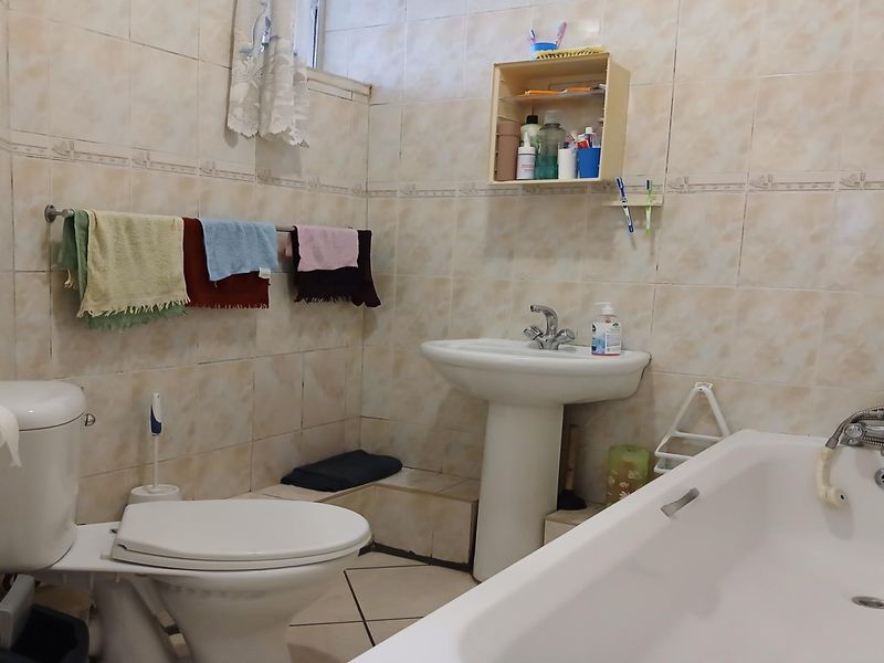 A functional bathroom featuring a pedestal washbasin, toilet, and bathtub with full-height wall tiling and tiled flooring.